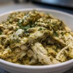 Shredded chicken coated in a creamy, green salsa verde sauce, served in a white bowl.