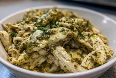 Shredded chicken coated in a creamy, green salsa verde sauce, served in a white bowl.