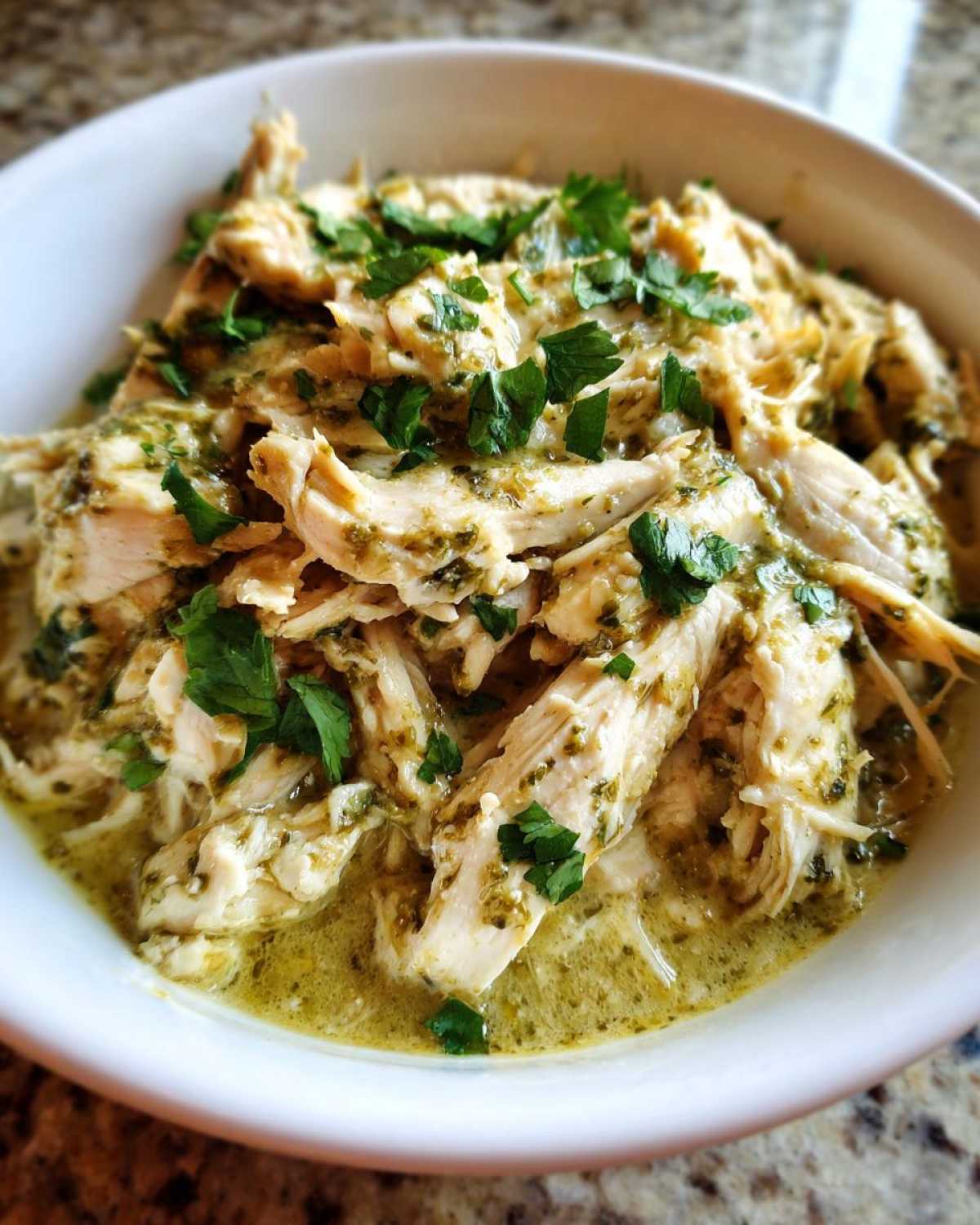 Close-up of shredded Easy One-Pot Creamy Salsa Verde Chicken served in a white bowl and topped with fresh cilantro.