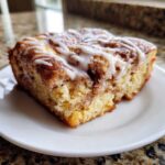 Close-up of a square slice of Easy Sheet Pan Cinnamon Roll Pancake Bake, drizzled with white icing.