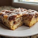 A square slice of Easy Sheet Pan Cinnamon Roll Pancake Bake drizzled with white icing on a white plate.