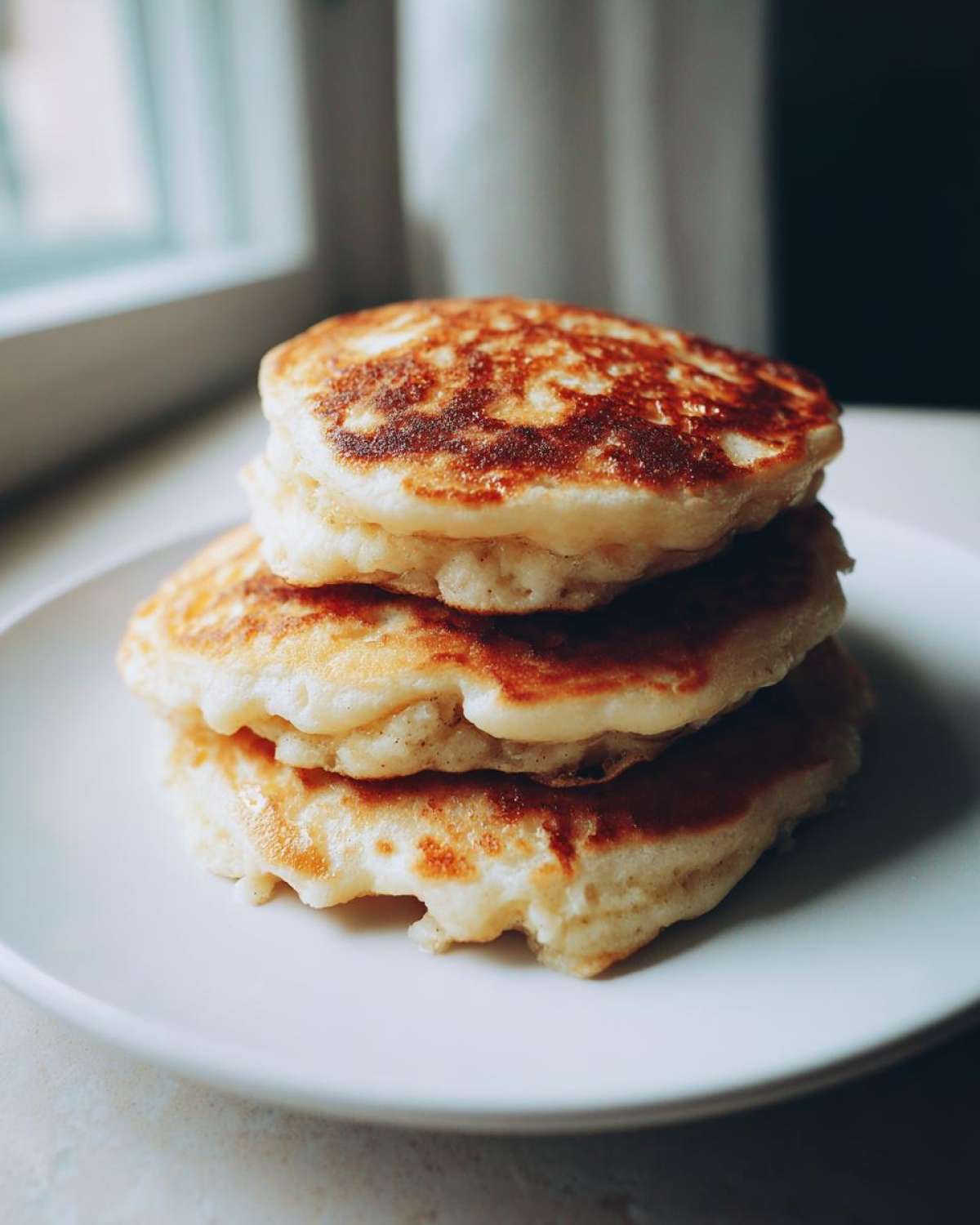 A close-up stack of three fluffy Banana Pancakes with golden-brown tops served on a white plate.
