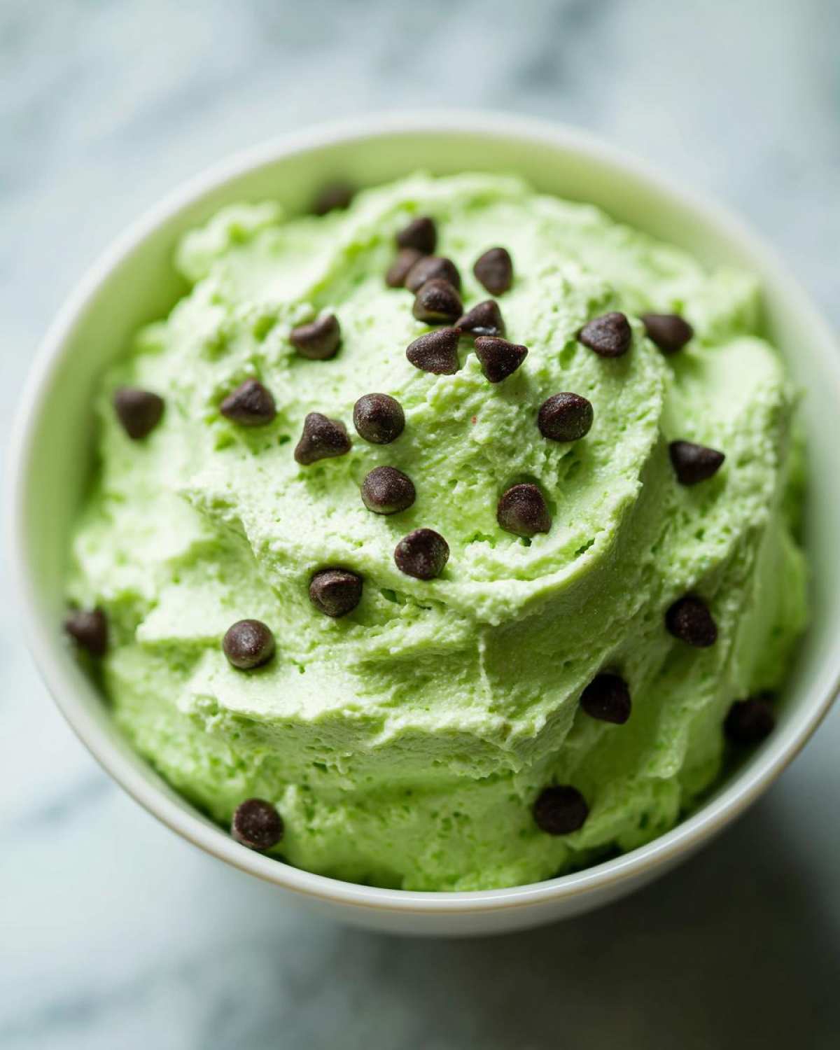 Close-up of bright green Grinch dip topped generously with mini chocolate chips in a white bowl.