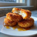 Stack of golden brown Fried Manchego Cheese rounds drizzled with honey, one piece broken open showing the soft white cheese.