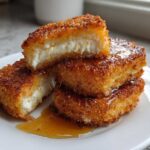 Close-up of golden brown Fried Manchego Cheese pieces stacked on a white plate, oozing with melted cheese and drizzled with honey.