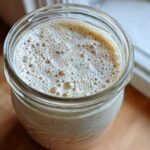 Overhead view of creamy chia seed pudding topped with a layer of light brown foam in a glass Ball jar.