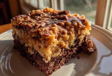 A close-up of a moist slice of german chocolate poke cake featuring a dark chocolate base and a gooey coconut-pecan topping.