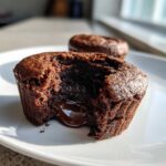 Close-up of a Gluten-Free Chocolate Lava Brownie Cup broken open, showing the rich, molten chocolate flowing out onto a white plate.