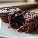 Close-up of a Gluten-Free Chocolate Lava Brownie Cup cut open, showing rich, molten chocolate flowing out onto a white plate.