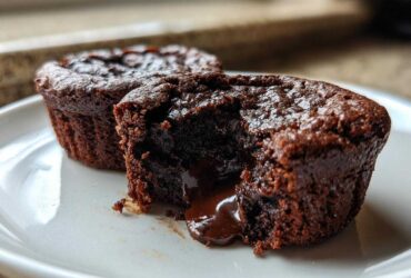 Close-up of a Gluten-Free Chocolate Lava Brownie Cup cut open, showing rich, molten chocolate flowing out onto a white plate.