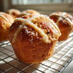 A close-up of a freshly baked Gluten-Free Hot Cross Bun Muffin topped with icing cross and coarse sugar.