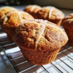 Close-up of a freshly baked Gluten-Free Hot Cross Bun Muffin with a piped cross and sugar crystals, cooling on a wire rack.