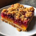 A square slice of Gluten-Free Lemon Berry Crumble Bars featuring a thick crust, bright lemon layer, berry filling, and crumb topping.