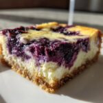 A close-up of a single serving of Gluten-Free Lemon Blueberry Cheesecake Squares showing the graham crust and creamy filling with swirls of blueberry.