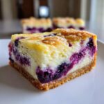 A close-up view of one square of Gluten-Free Lemon Blueberry Cheesecake Squares showing the creamy filling, blueberries, and crumb topping.