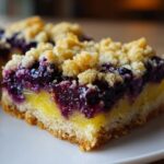A close-up shot of a square slice of Gluten-Free Lemon Blueberry Layer Bars showing the crumbly base, bright lemon filling, and dark blueberry topping.