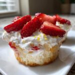 A close-up of a Gluten-Free Lemon Strawberry Angel Food Cup topped with whipped cream and fresh sliced strawberries.