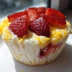 A single Gluten-Free Lemon Strawberry Angel Food Cup topped with fresh sliced strawberries, sitting on a white plate.