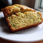 Close-up of a thick slice of moist Gluten-Free Lemon Zucchini Bread showing green zucchini shreds and yellow zest.
