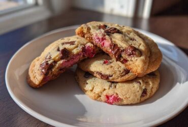 A stack of warm Gluten-Free Strawberry Chocolate Chip Cookies, one broken open showing melted chocolate and pink strawberry filling.