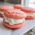A close-up of one Gluten-Free Strawberry Lemon Whoopie Pie filled with thick white cream, with others blurred in the background.