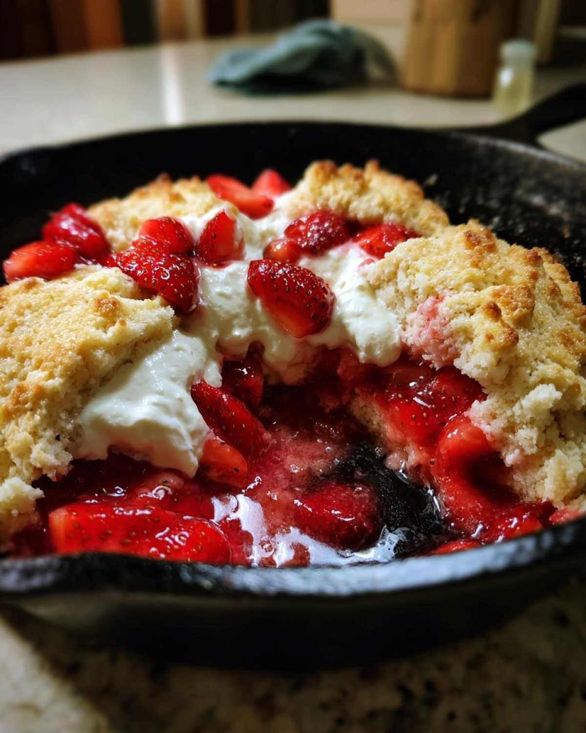 Close-up of warm Gluten-Free Strawberry Shortcake Skillet with juicy strawberries and whipped cream in a cast iron pan.