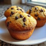 Three freshly baked, golden-brown chocolate chip muffins resting on a white plate.