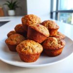 A stack of freshly baked, golden brown mini banana muffins piled high on a white plate.