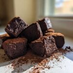A stack of rich, dark Greek Yogurt Chocolate Banana Brownie Bites dusted with cocoa powder.