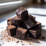 A stack of rich, dark Greek Yogurt Chocolate Banana Brownie Bites dusted with cocoa powder.