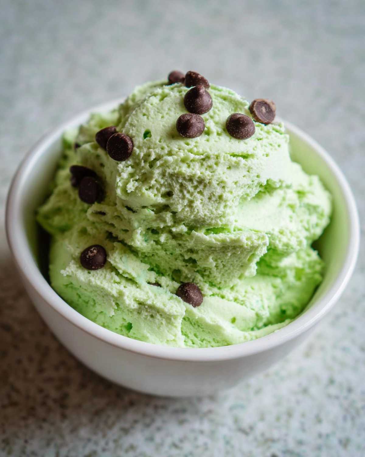 A close-up of a scoop of bright green Grinch dip, topped with mini chocolate chips, served in a white bowl.