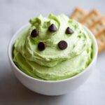 A white bowl filled with fluffy, bright green Grinch dip, topped with dark chocolate chips.