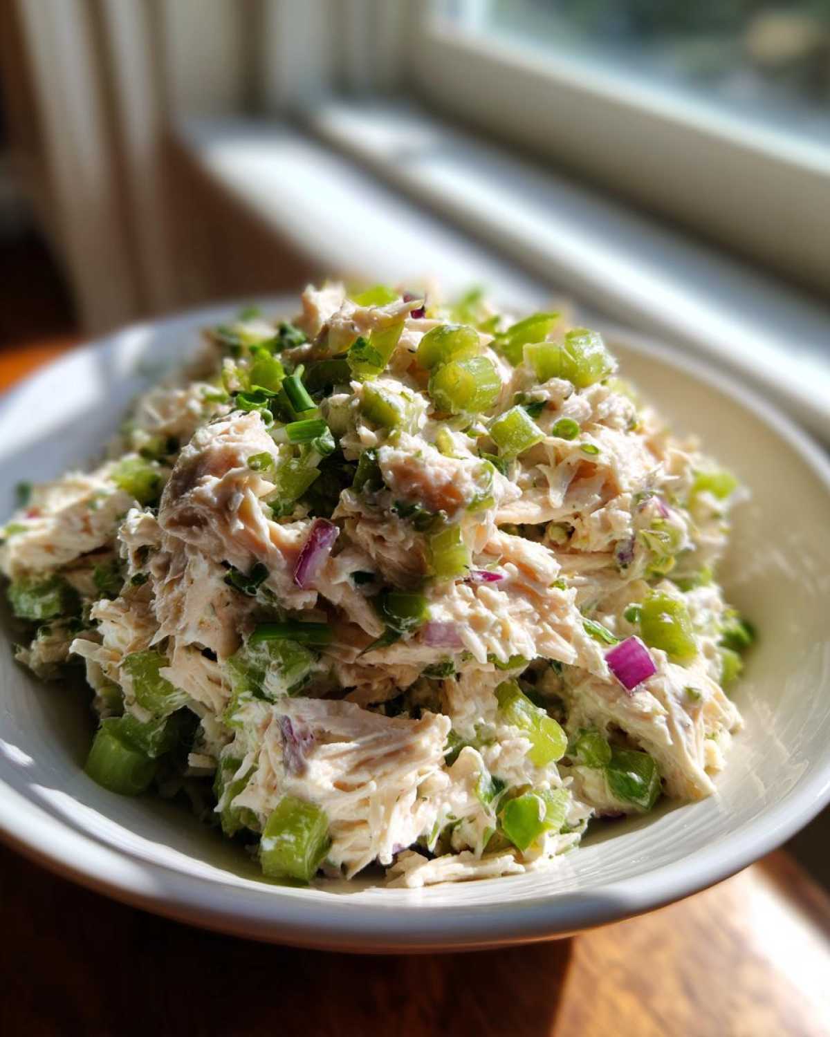 Close-up of a bowl filled with creamy high protein chicken salad, featuring shredded chicken, bright green celery, and red onion.
