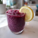 Close-up of a vibrant, deep purple Iced Blueberry Lemonade Slush garnished with a fresh lemon slice.