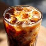 Close-up of a tall glass filled with Iced Brown Sugar Cinnamon Cold Brew, showing ice cubes and swirling cream/milk.
