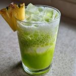 A bright green Iced Pineapple Matcha Spritz served over ice, garnished with a pineapple wedge.