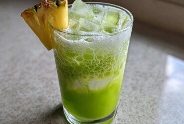 A bright green Iced Pineapple Matcha Spritz served over ice, garnished with a pineapple wedge.