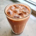 Close-up of a tall glass filled with Iced Raspberry Vanilla Chai, topped with ice cubes and light foam.