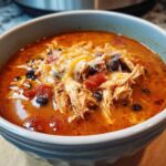 Close-up of a bowl of Instant Pot Creamy Chicken Enchilada Soup topped with shredded chicken, black beans, tomatoes, and melted cheese.