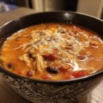 A close-up of a bowl of Instant Pot Creamy Chicken Enchilada Soup topped with shredded cheese.