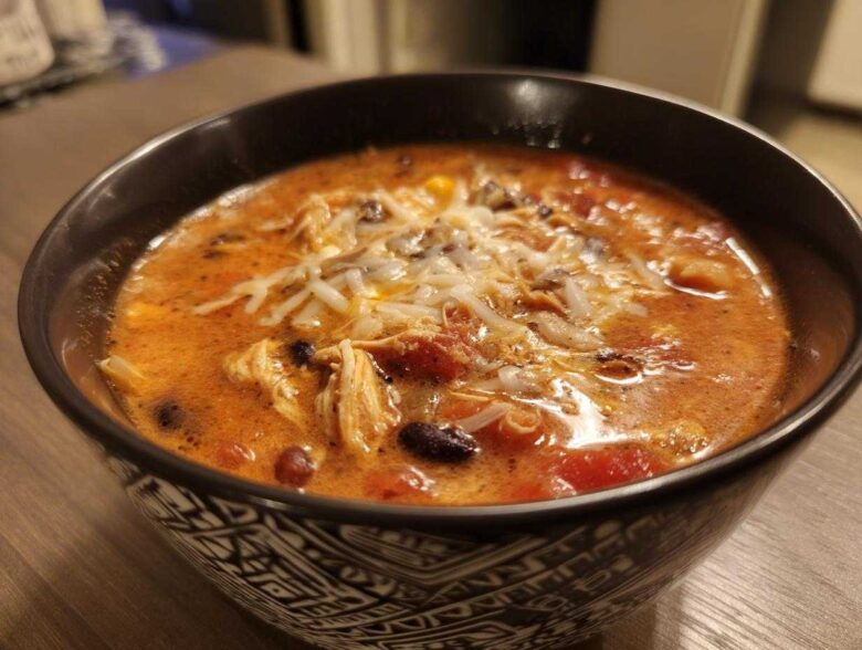 A close-up of a bowl of Instant Pot Creamy Chicken Enchilada Soup topped with shredded cheese.