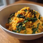 A white bowl filled with vibrant orange Instant Pot Creamy Coconut Lentils with Spinach.