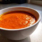 Close-up of a white bowl filled with vibrant orange Instant Pot Creamy Red Pepper Tomato Soup.
