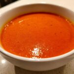 Close-up of a white bowl filled with vibrant orange Instant Pot Creamy Red Pepper Tomato Soup.