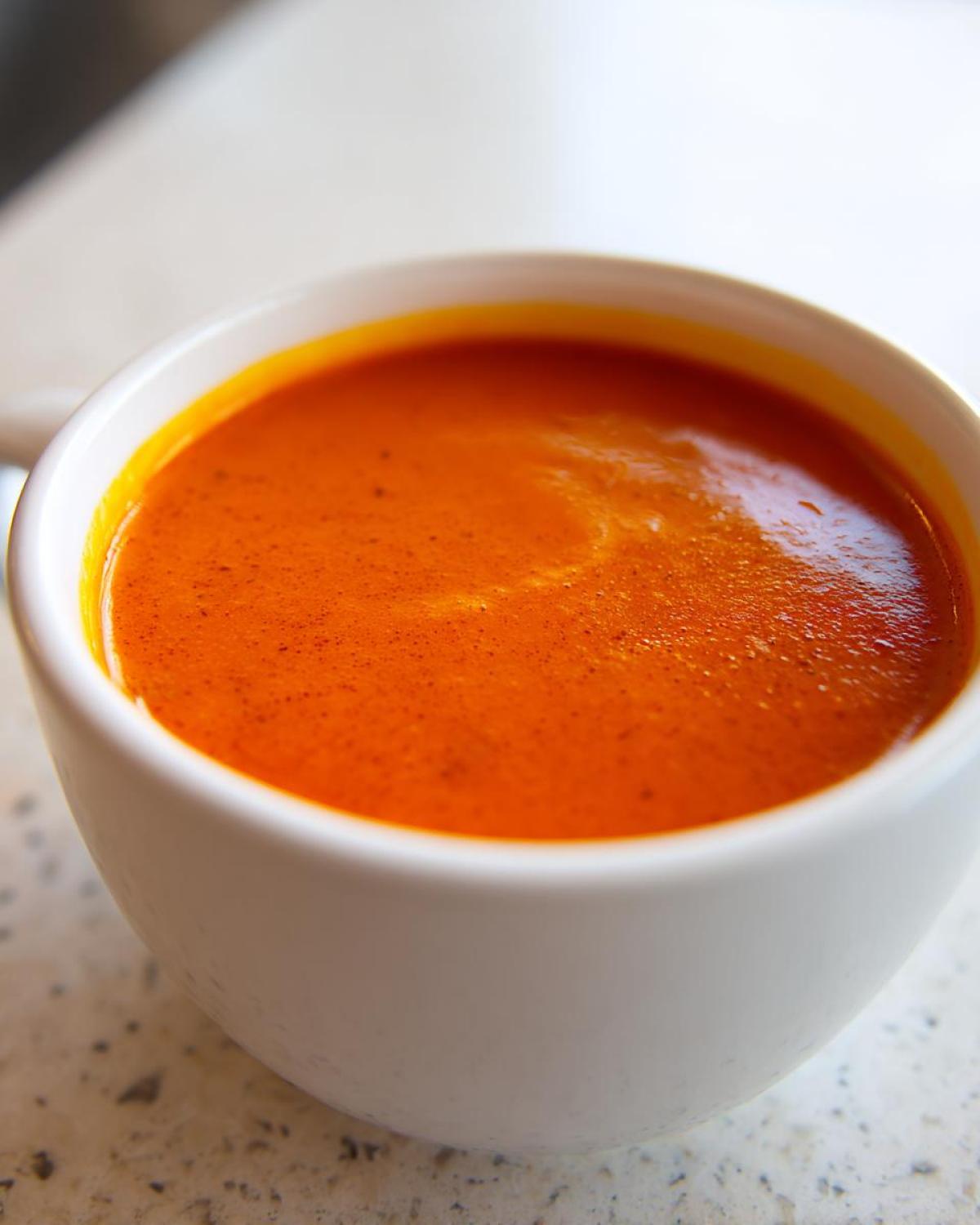 A close-up shot of vibrant orange Instant Pot Creamy Red Pepper Tomato Soup served in a white mug.