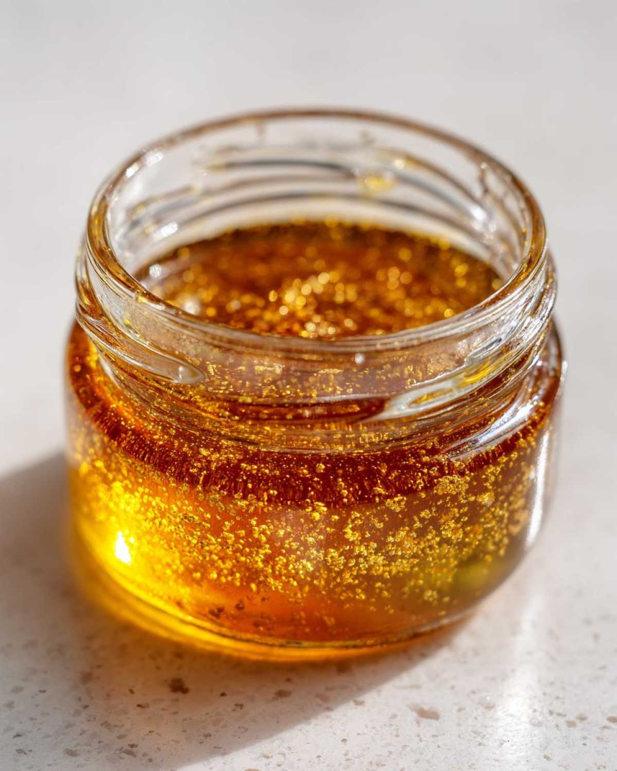 Close-up of a small glass jar filled with golden, shimmering Copycat Apple Cider Vinaigrette.