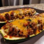 Two baked Keto Cheesy Taco Stuffed Zucchini Boats filled with seasoned ground meat and topped with melted cheddar cheese.