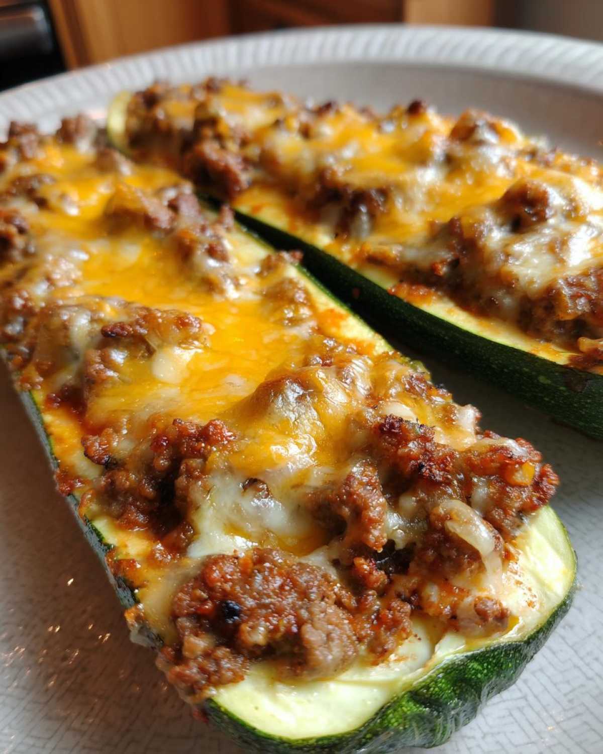 Close-up of two Keto Cheesy Taco Stuffed Zucchini Boats topped with browned taco meat and melted cheddar cheese.