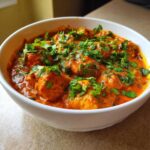 Close-up of a white bowl filled with rich, orange-red Keto Creamy Butter Chicken Skillet, topped generously with fresh cilantro.