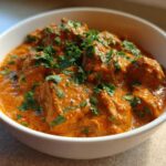 A close-up of rich, orange-red Keto Creamy Butter Chicken Skillet served in a white bowl and garnished with fresh cilantro.